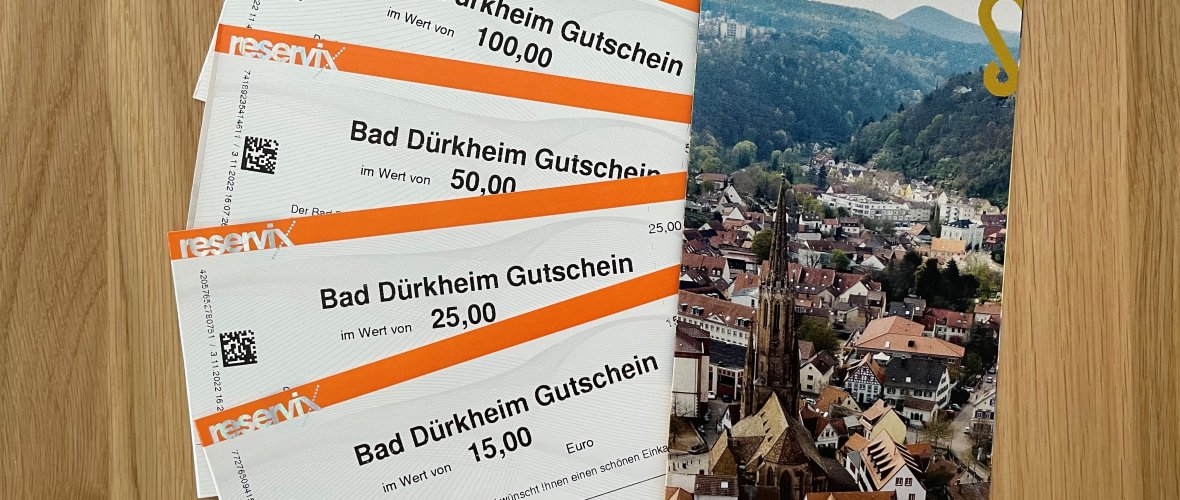 Zu sehen sind aufgefächert vier Bad Dürkheim Gutscheine in den Preiskategorien 15€, 25€, 50€ und 100€. Daneben der Gutscheinflyer von vorne.